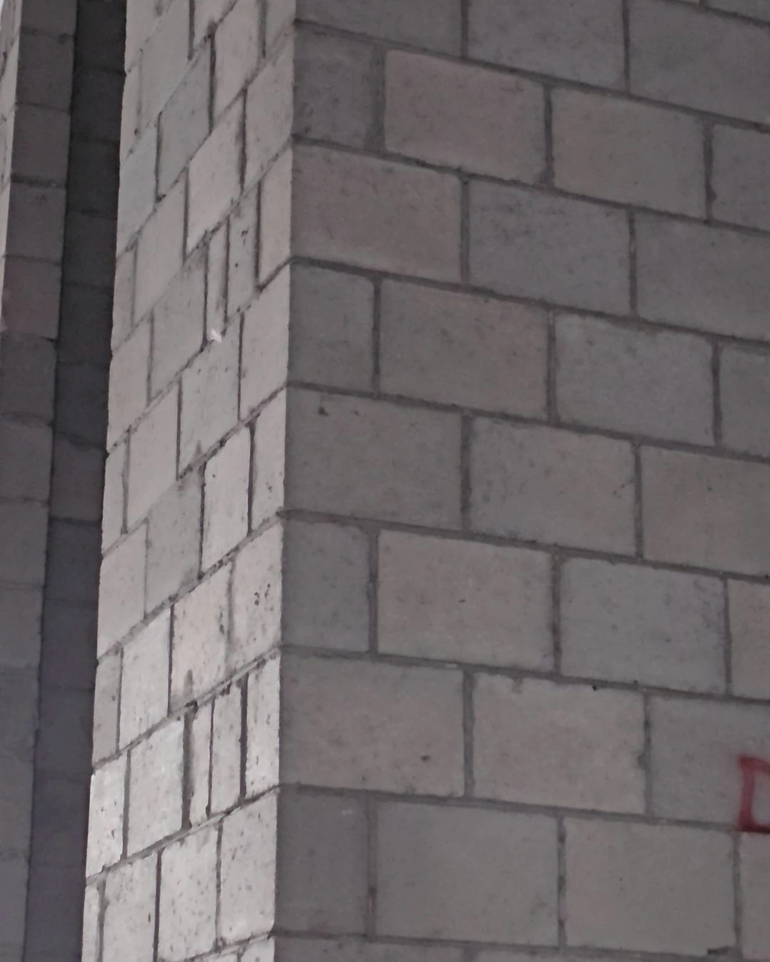 Close-up of a building corner constructed with light gray concrete blocks, showing mortar joints and a vertical structural column gap.