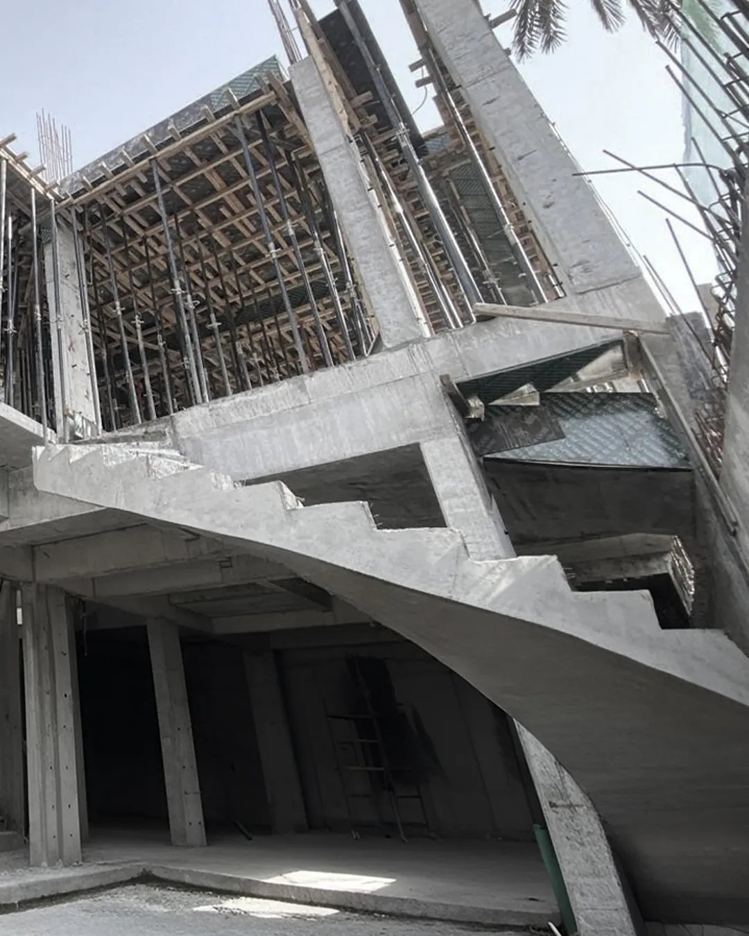 Reinforced concrete structure featuring a curved staircase, vertical columns, and upper-level slab formwork supported by dense scaffolding.