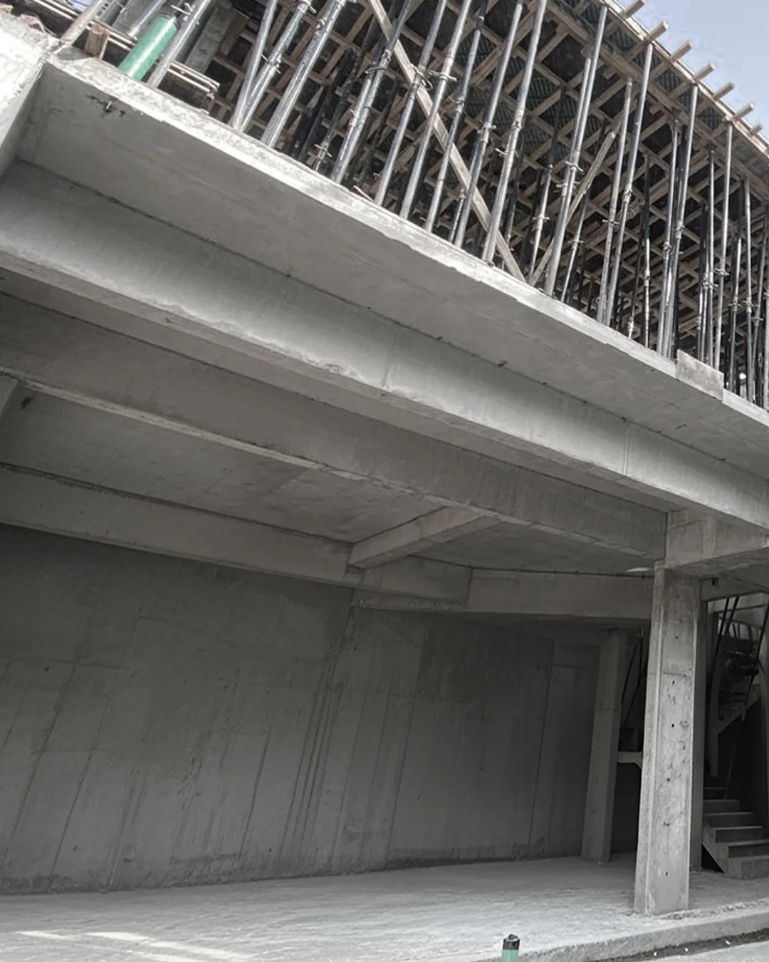 Reinforced concrete building structure showing lower-level columns and beams with upper-level slab formwork and scaffolding still in place.
